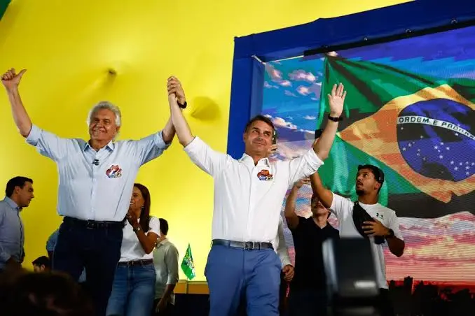 Ronaldo Caiado e Flávio Bolsonaro de mãos dadas e braços erguidos em um palco
