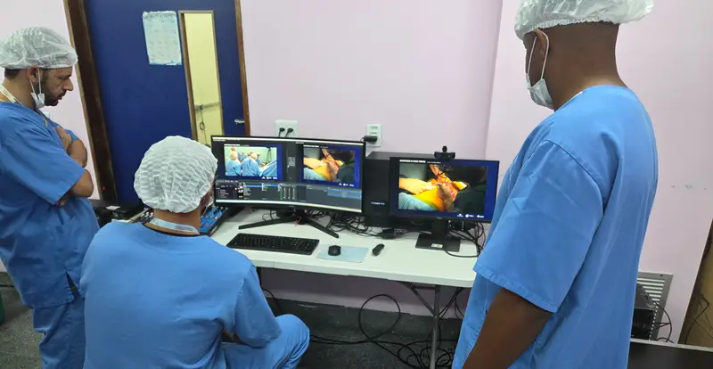 Cirurgiões de touca acompanhando imagens em monitores