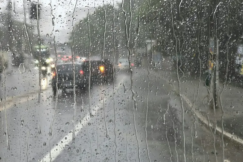 Gotas de chuva no vidro, com carros em uma avenida ao fundo