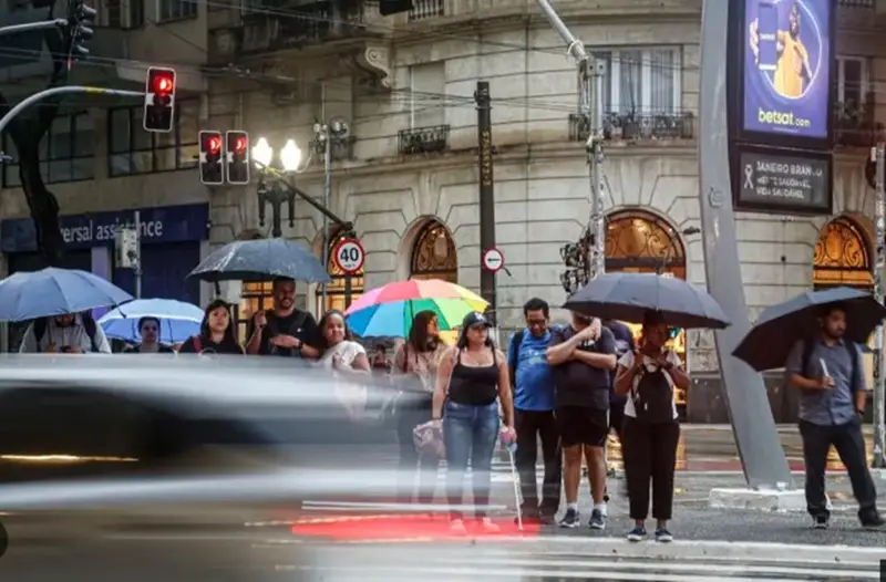 Pedestres com guarda-chuvas atravessando uma rua no centro da cidade