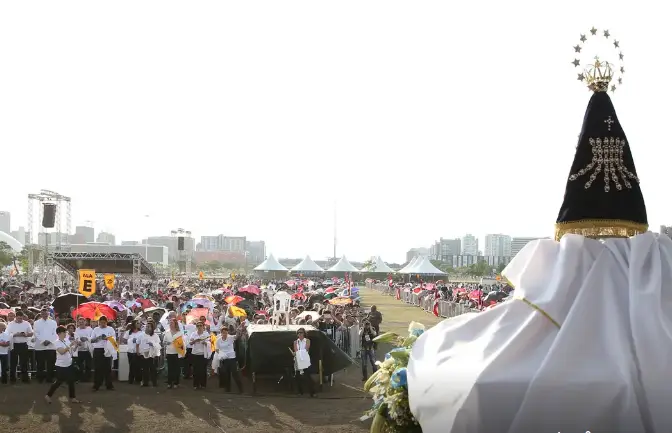 Imagem de Nossa Senhora Aparecida diante de multidão de fiéis em uma celebração ao ar livre
