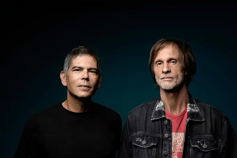 Dois músicos posando em fundo escuro