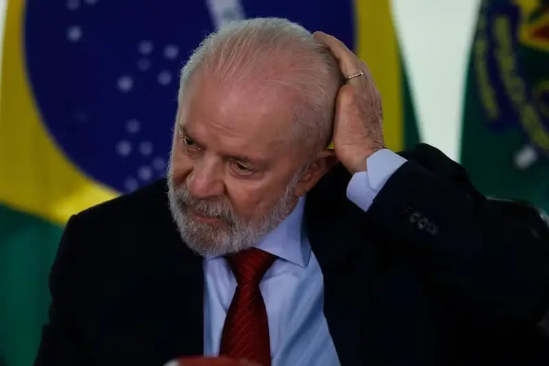 Lula com a mão na cabeça diante da bandeira do Brasil