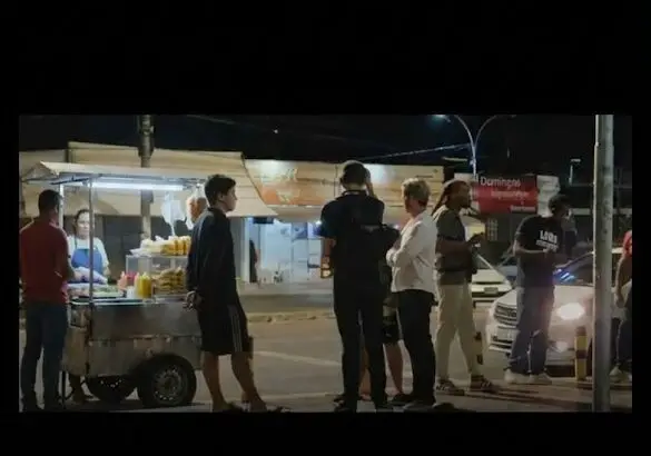 Pessoas reunidas à noite ao lado de um carrinho de lanches na calçada