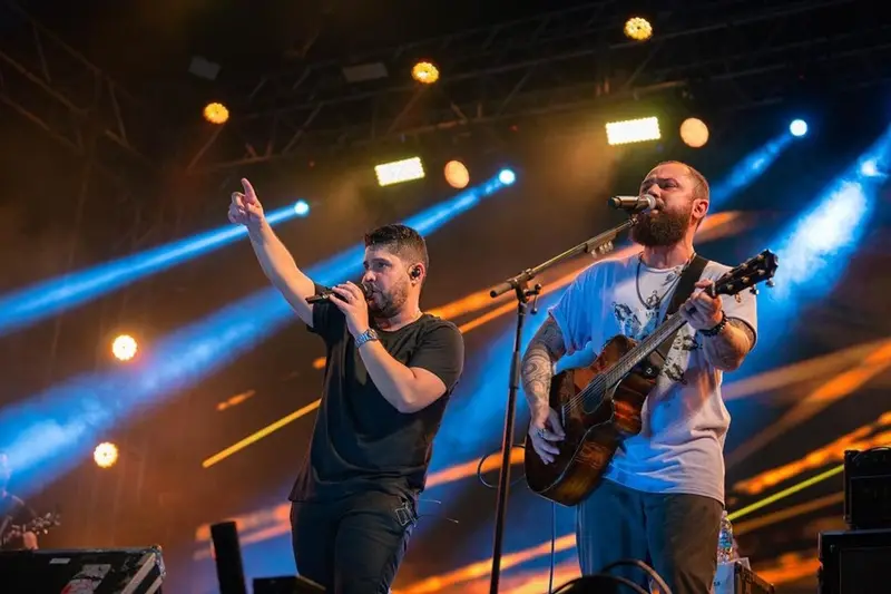 Dupla cantando e tocando violão sob luzes coloridas