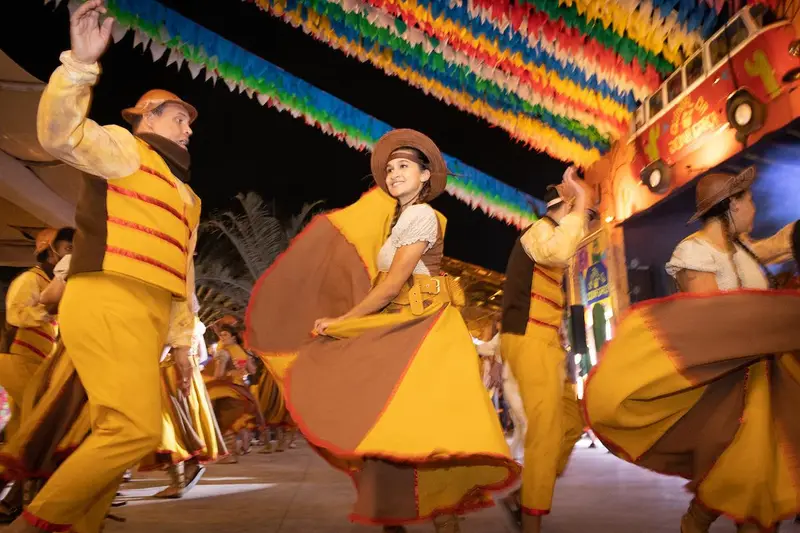 Dançarinos de quadrilha com roupas amarelas sob bandeirinhas