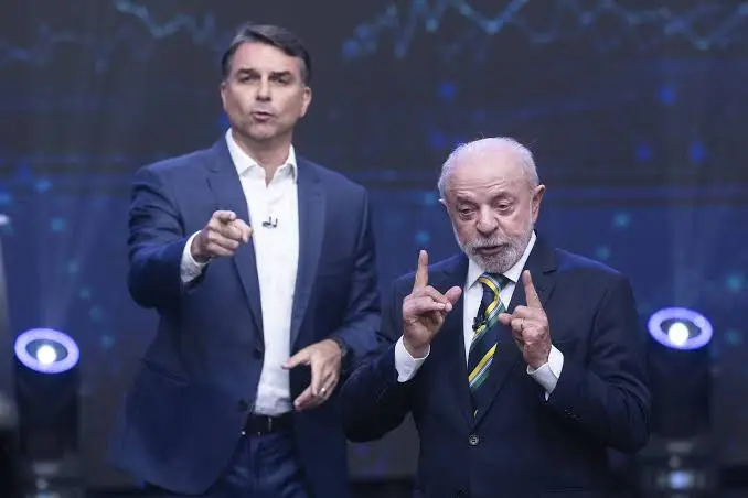 Flávio Bolsonaro e Lula gesticulando no estúdio do debate na TV