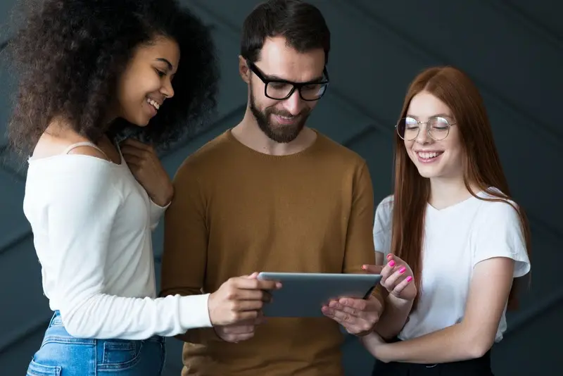 Três jovens sorrindo e olhando um tablet