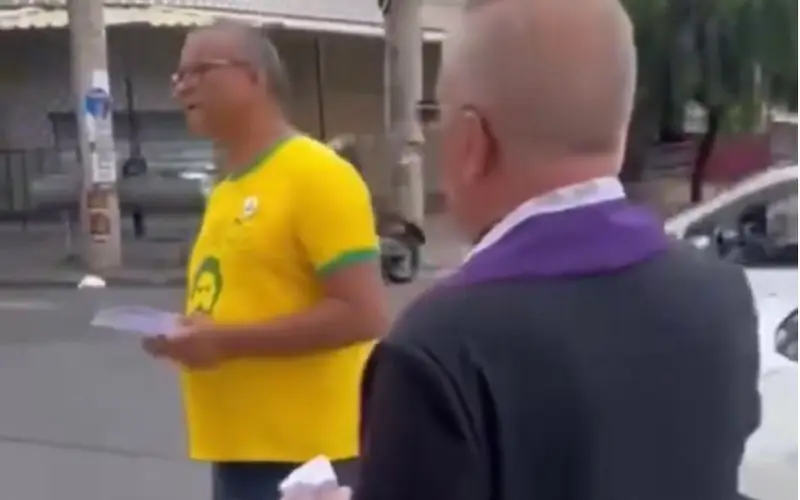 Homem de camisa amarela distribuindo panfletos ao lado de um padre na rua