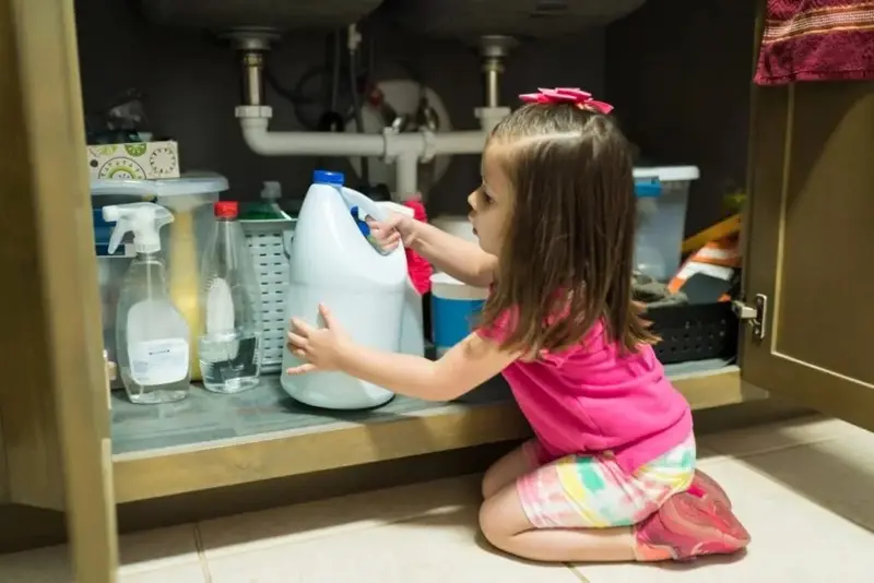 Menina mexendo em produtos de limpeza no armário da cozinha