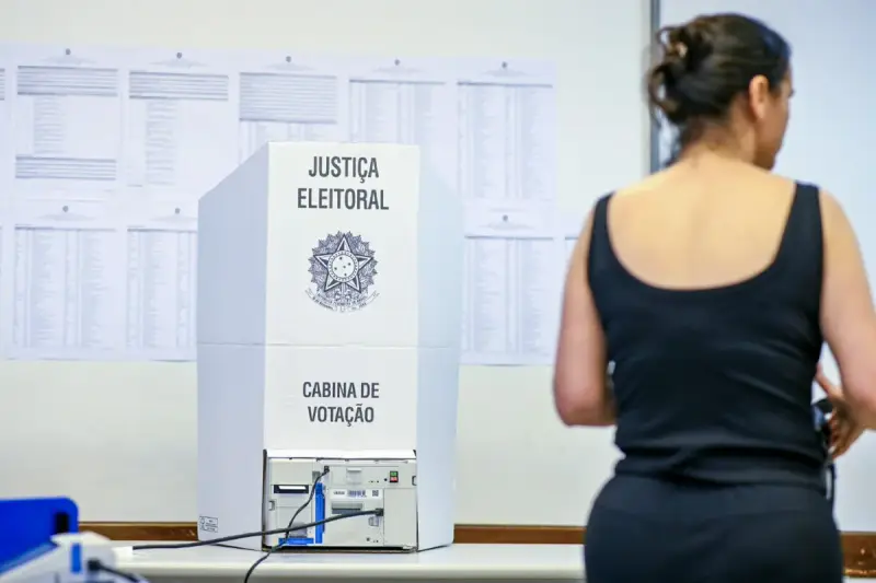 Mulher de costas diante de uma cabine de votação da Justiça Eleitoral