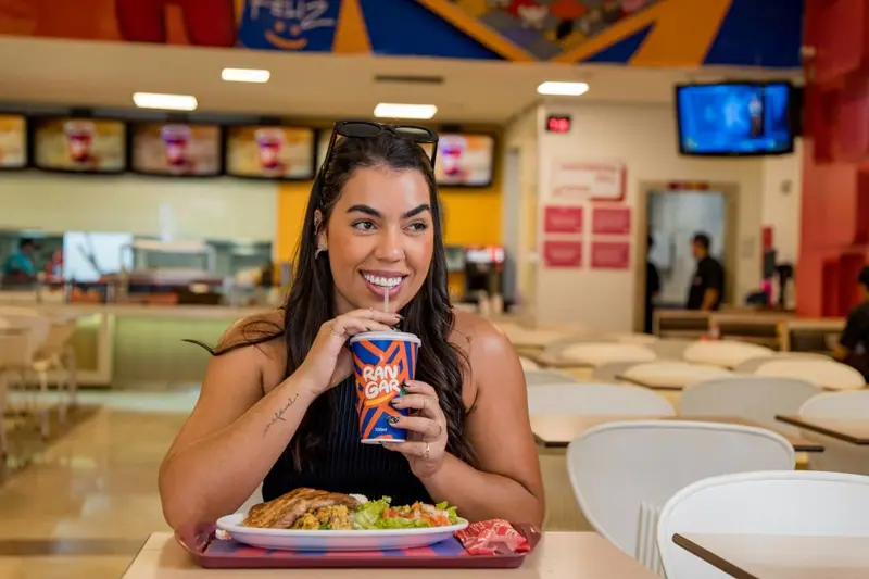 Mulher sorrindo com copo e prato de comida em uma lanchonete