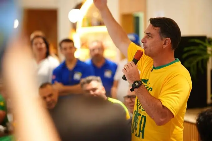 Flávio Bolsonaro de camisa amarela falando ao microfone para apoiadores