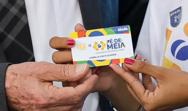 Mãos segurando o cartão do programa Pé-de-Meia