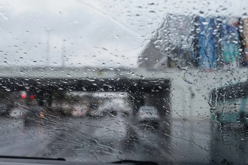 Gotas de chuva no para-brisa, com o trânsito ao fundo