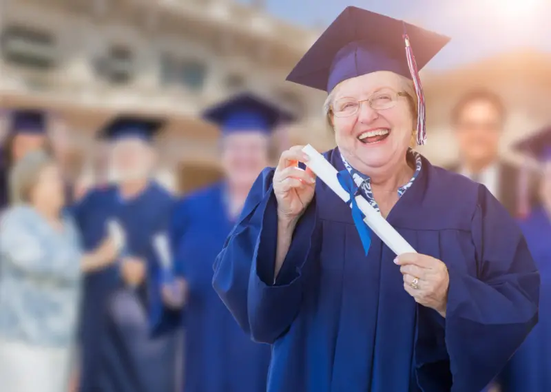 Senhora sorridente de beca e capelo segurando um diploma